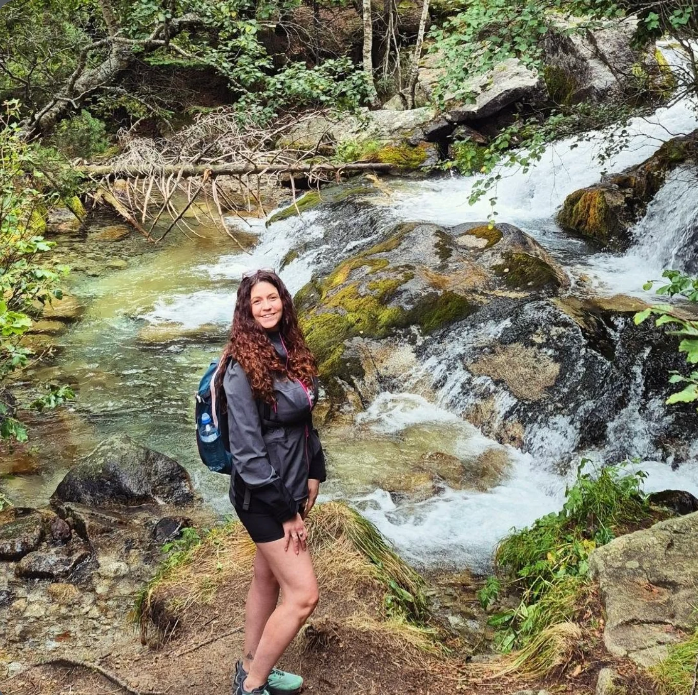 Yasmin junto a un arroyo entre rocas y vegetación